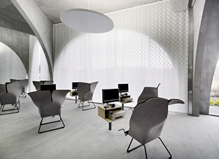 Grau gehaltener großzügiger raum mit modernen grauen Stühlen. An der Fensterfront ein Schleuderzugsystem mit weißem Stoff.