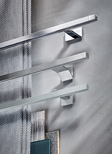 Designbeispiel von drei Gardinenschienen, quadratisch montiert auf hellgrauer Wand mit verschiedenen Haltern. Oben verchromt, Mitte gebürsteter Edelstahl und unten matt.