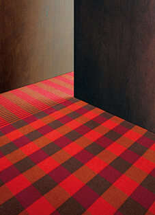 Webteppichboden "Check4stripes" von Tisca Tiara für den Objektbereich. Der gewebte Teppich zeigt ein großes Karomuster in Rot- und Brauntönen, das in einer Ecke in ein Streifenmuster übergeht.