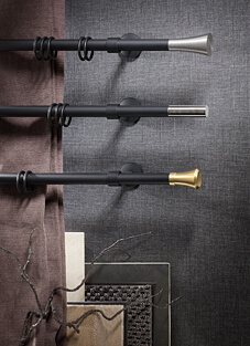 Designbeispiel von drei Gardinenstangen, montiert auf dunkelgrauer Wand. In schwarz mit Ringen darauf und verschiedene Endstücke. Oben Silber matt konisch auslaufend, Mitte Silber geradlinig, Unten Golden konisch auslaufend.