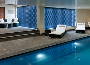 Ausschnitt einer modernen Schwimmhalle. im Vordergrund Schwimmbecken, dahinter am Beckenrand Ruheliegen. Im Hintergrund Vertikal Waves in Blau mit Elektroantrieb.