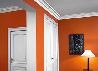 Zimmerdurchbruch in weißer Laibung und orangenen Wänden. Stilvoll umrahmt von zeitlosen Deckenleisten.