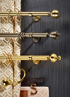 Designbeispiele von drei Gardinenstangen mit Ringen darauf, montiert auf einer dunkelgrauen Wand. Von oben nach Unten: Messing mit Kugel als Endstück, Mittig brüniert mit einem konisch zulaufendem Endstück. Unten golden mir rundem Endstück.
