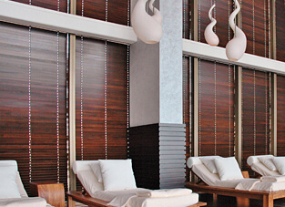 Ausschnitt von einem Spa. Hölzerne Liegen mit weißen Matratzen, Kissen und Decken. Dahinter Fensterfront mit dunklen hölzernen Jalousien.