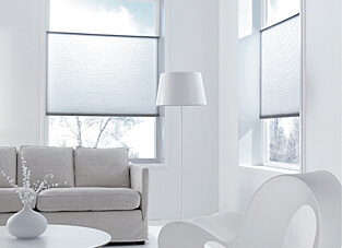 Ausschnitt eines weiß gehaltenem Wohnraum. An den Fenstern Plissees.