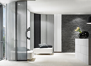 Moderner Wohnbereich in schwarz, grau und weiß. Links eine Fensterfront mit zwei weißen Sitzgelegenheiten die von einem gebogenen grau, weiß, schwarzen Flächenvorhangsystem umgeben sind.