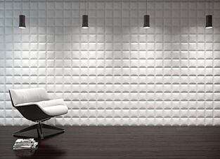 Raumausschnitt mit dunklem Boden, einem weißen Sessel, kleiner weißer Bücherstapel daneben und vier kleinen schwarzen Pendelleuchten vor weißer Wand aus quadratischen 3D Wandpaneelen.