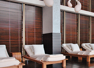 Ausschnitt von einem Spa. Hölzerne Liegen mit weißen Matratzen, Kissen und Decken. Dahinter Fensterfront mit dunklen hölzernen Jalousien.