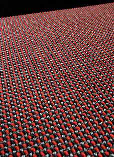 Nahaufnahme eines gewebten Teppichbodens von Tisca Tiara aus der Kollektion "Spectra". Die Textur ist ein zweichörig gewebtes Muster in dualer Optik, das aus vielen kleinen, eng beieinander liegenden Schlaufen in den Farben Schwarz, Rot und Hellgrau besteht. Die Aufnahme betont die feine, dichte Webstruktur, die auf beste Licht- und Farbechtheit und ausgezeichnete Verschleißfestigkeit hindeutet.