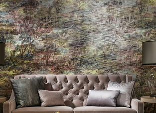 Eine elegante Szene mit einem gepolsterten, beigefarbenen Samtsofa mit Knopfheftung, das mit verschiedenen Grautönen und Kissen dekoriert ist. Die Wand dahinter ist mit einer textilen Wandtapete versehen, die ein großformatiges, historisch inspiriertes Wandbild (Mural) in gedämpften Farben wie Olivgrün, Braun und Rostrot zeigt, das einer Landschaft oder einem Wald ähnelt und eine strukturierte, verwaschene Optik aufweist.
