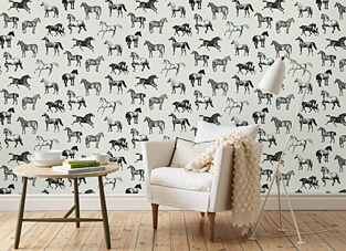 Designbeispiel einer Tapete. Wand mit weißem Untergrund und schwarzen Abbildungen von Pferden. davor auf hellem Holzboden ein kleiner hölzerner Beistellstich mit Büchern und Geschirr darauf. Rechts weißer Sessel mit Kissen und Decke darauf. Rechts eine moderne weiße Stehlampe.