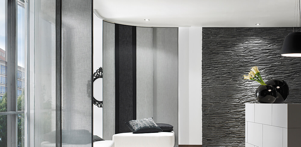 Designbeispiel der Vorhangschienen von Silent Gliss. Schwarz, grau, weiß gehaltener Raum mit weiß, grau und schwarzen Paneelen vor der Fensterfront.